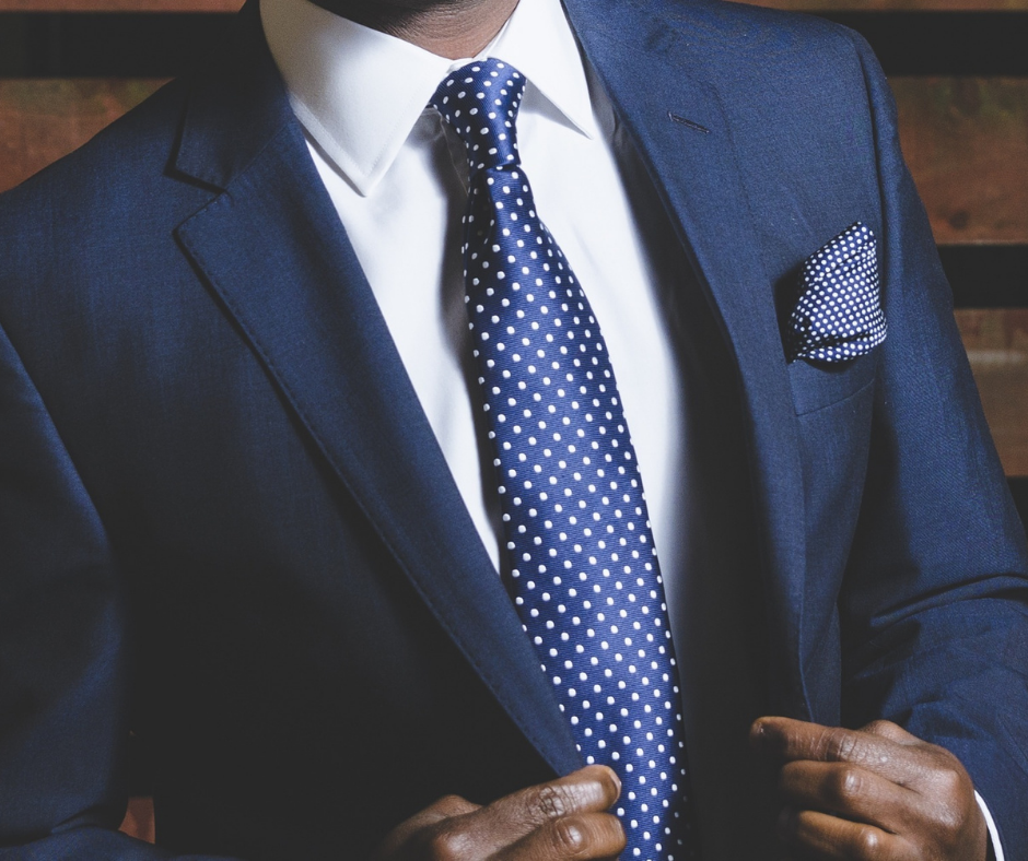 What makes a garment wrinkle-free? Man in a navy suit with a crisp white dress shirt, navy tie, and pocket square